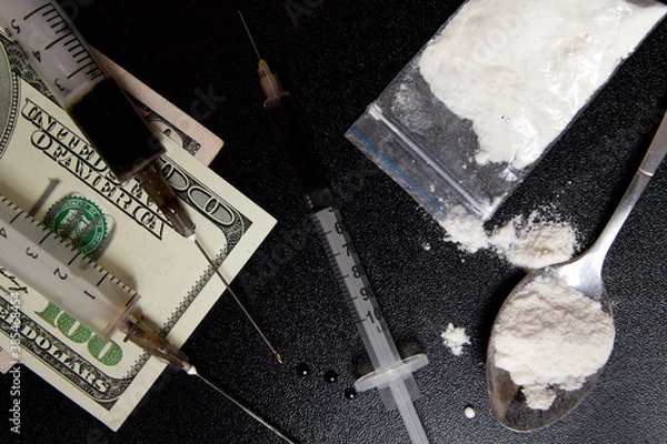 Fototapeta The use of drugs. Syringe with liquid, powder drugs and a tablespoons of prepared for heroin and money dollars on a dark background.