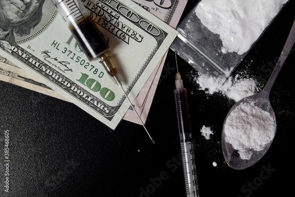 Fototapeta The use of drugs. Syringe with liquid, powder drugs and a tablespoons of prepared for heroin and money dollars on a dark background.