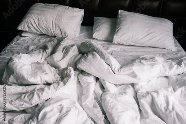 Fototapeta Unmade empty bed with white linens. Sheets and pillows in the apartment or hotel after a night's sleep. Dirty and crumpled blanket in the hotel