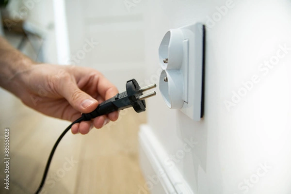 Fototapeta Inserting the plug into an electric socket in a bright interior, focus and close-up on a socket.