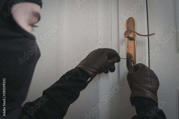 Fototapeta Burglar holding Lock-picker to open a housedoor. Home Burglar in a Mask Breaking Into the House. House Thief Concept Photo
