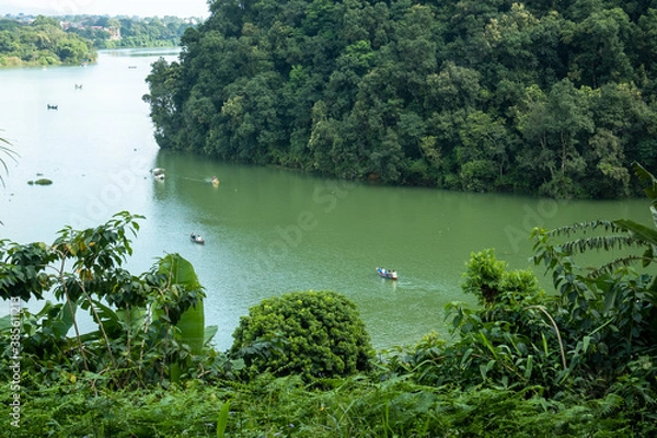 Fototapeta View of a tropical lake surrounded by lush green vegetation. Many small boats with tourists float on the surface of the water