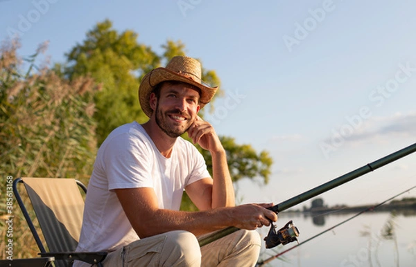 Fototapeta A smiling man is fishing and enjoying the peace at the river.