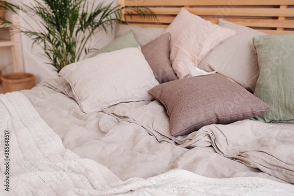 Fototapeta very cozy soft pastel place to relax and sleep. Pillows in soft maroon and green, rumpled knitted beige blanket on large bed. Selective focus