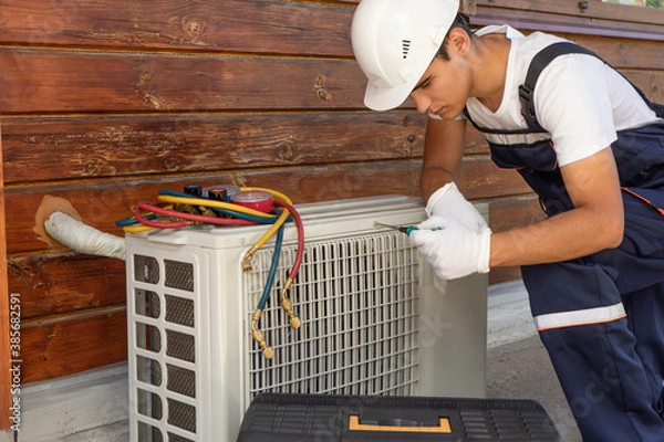 Obraz A young master in a white construction helmet repairs air conditioning, installation of split systems and maintenance of home heating