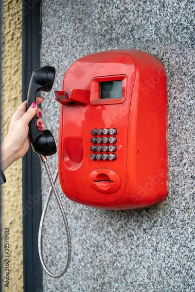 Fototapeta Woman using a public red telephone reaching out with her hand to take the handset off the cradle