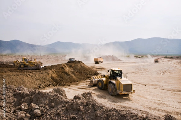 Fototapeta Earthworks in an open area on a summer sunny day. Cargo dump trucks, excavators, wheel loaders and bulldozers operate at the same time.