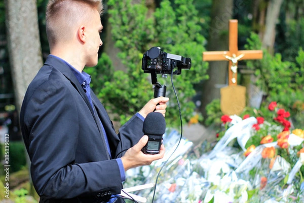 Obraz The professional man transmitting the funeral live. Funeral recording. Cameraman at the cemetery recording the burial. Funerals online. Funerals live.
