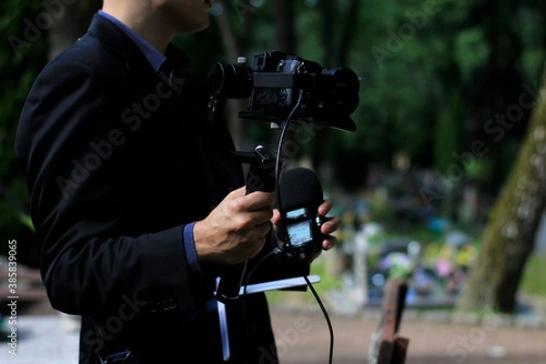 Obraz The professional man transmitting the funeral live. Funeral recording. Cameraman at the cemetery recording the burial. Funerals online. Funerals live.