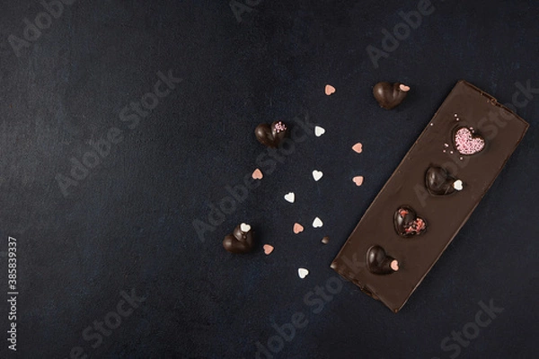 Obraz Dark chocolate bar with decorations isolated on a dark background. Top view, flat lay. Free space for text.