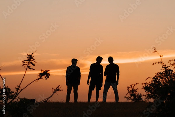 Fototapeta Silhouette of three Indian friends standing in front of the sky during the sunset