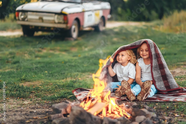 Obraz Two cute little girls sitting by a bonfire on summer evening in forest.