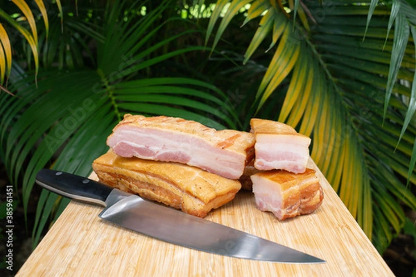 Fototapeta Smoked bacon. Cold cuts on a wooden board with palm background