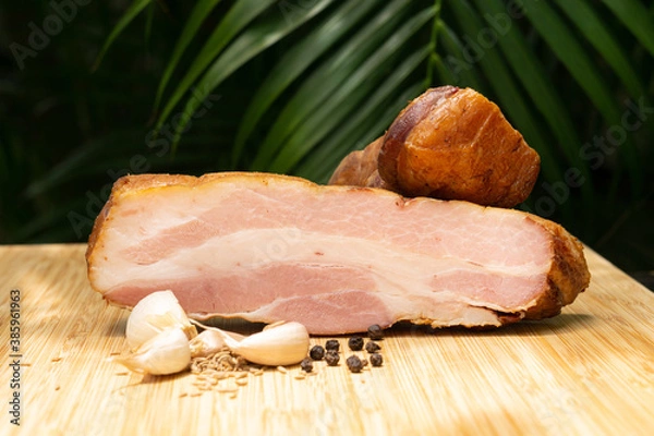 Fototapeta Smoked bacon. Cold cuts on a wooden board with garlic, cumin and black pepper