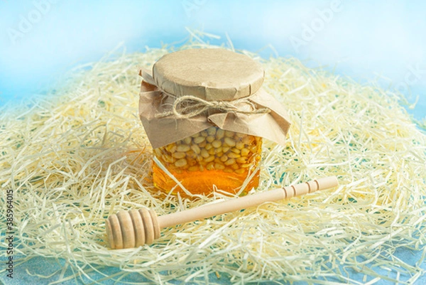 Fototapeta Jar of honey with nuts and honey spoon in a wooden box with sawdust, top view