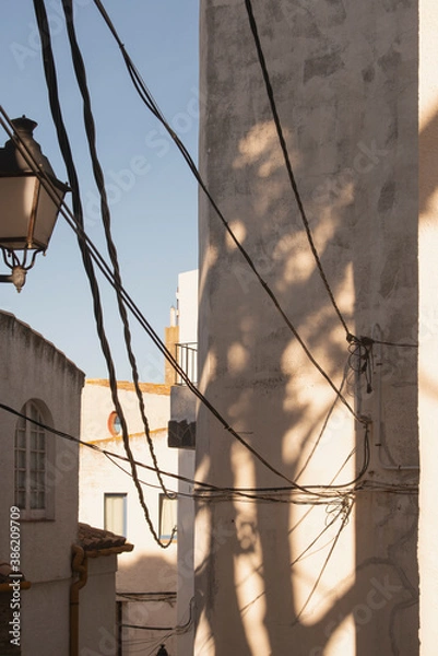 Fototapeta typical Cadaques, Girona, Spain alley at summer with blue sky, white houses, lamp post, and wires on a sunny afternoon