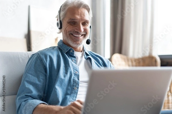 Fototapeta Smiling man in headset watch webinar or training on modern computer, male call center agent or telemarketer work consult client online