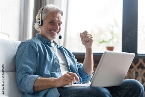 Fototapeta Smiling man in headset watch webinar or training on modern computer, male call center agent or telemarketer work consult client online