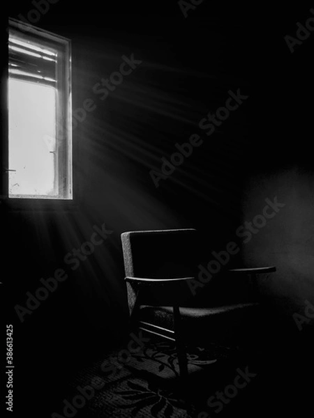 Fototapeta Dramatic room in abandoned house with an old empty chair near the window, black and white image. Light coming from the window, vertical shot.