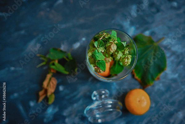 Fototapeta Glass vase stands on the table, it has tangerines and leaves around, the view from above (without lid).