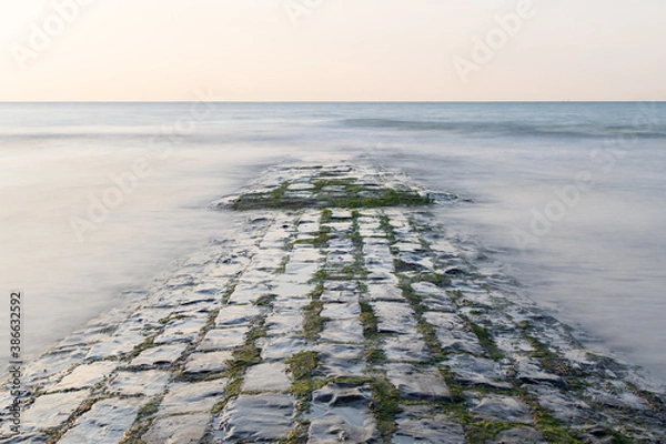 Obraz A wet stone breakwater is half submerged in blurred waters.