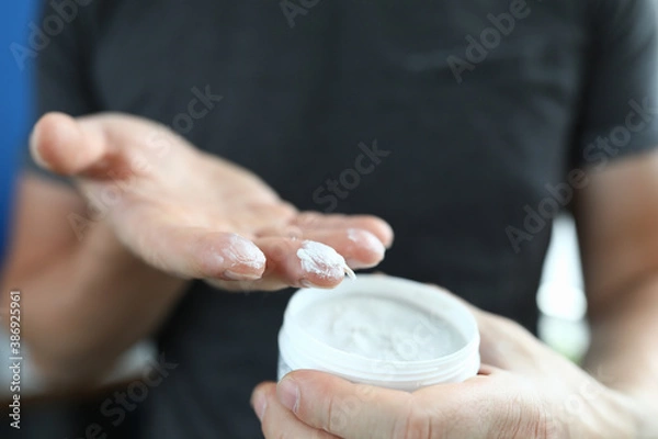 Obraz Man's hand holds jar with a white substance inside. Cosmetics for men concept