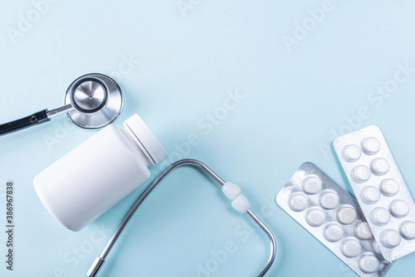 Fototapeta Black stethoscope and pills on blue background. Medical tool for diagnostic coronavirus disease. Medicine and healthcare concept. Copy space for text