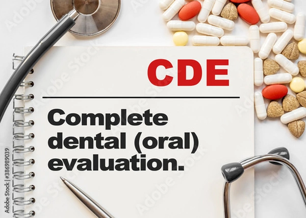 Fototapeta Page in notebook with CDE Complete dental oral evaluation. on white background with stethoscope and group of pill. Medical concept. Term and abbreviation