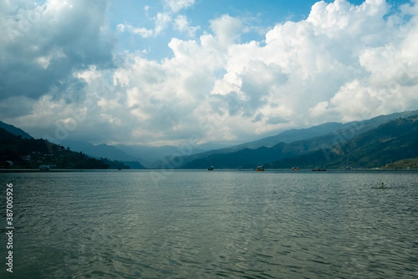 Fototapeta View of the lake with turquoise water and the opposite mountain shore. Reflection of clouds in calm water. Phewa Lake in Pokhara (Nepal) in the evening