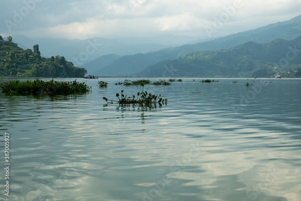 Fototapeta Waves on the surface of the lake water. Buildings on the shore. In the distance, the mountains are lost in the fog. Massive clouds above them