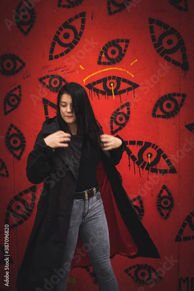 Fototapeta A girl on a red background. Brunette in black cape