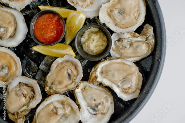 Obraz Oysters on the half shell. Fresh oysters served with garlic, shallots, cocktail sauce, mignonette sauce and fresh lemons and limes. Classic American steakhouse or French bistro appetizer.