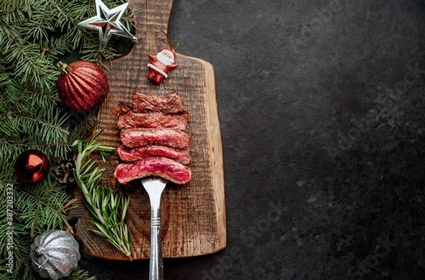 Obraz Different degrees of roasting of steak on a meat fork for Christmas on a background of a stone with a spruce and Christmas toys with copy space for your text