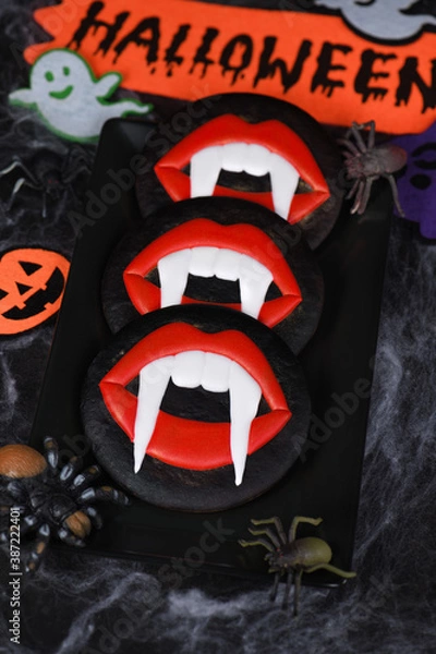 Fototapeta Vampire fangs protruding from scarlet lips, Glazed honey gingerbread cookies. Halloween food idea