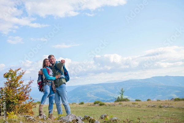 Fototapeta Two hikers with backpack standing on top of a mountain and look