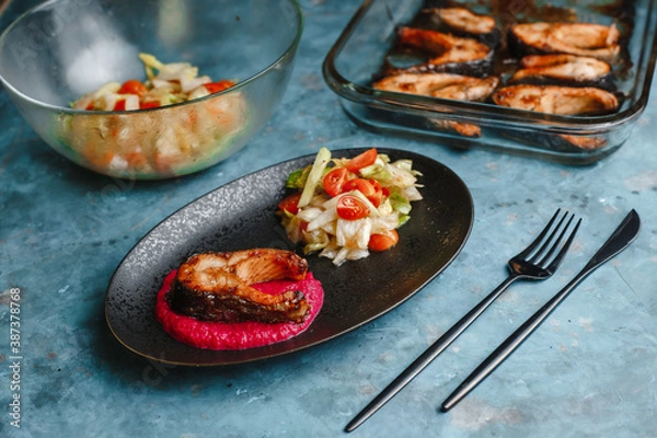 Fototapeta Trout. Baked salmon steaks on a beetroot pillow with vegetable salad, cucumber, tomato, onion, lettuce. Side view, top view.