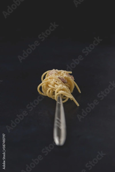 Obraz Fork of traditional Italian dish spaghetti carbonara isolated on dark background. Close-up view.