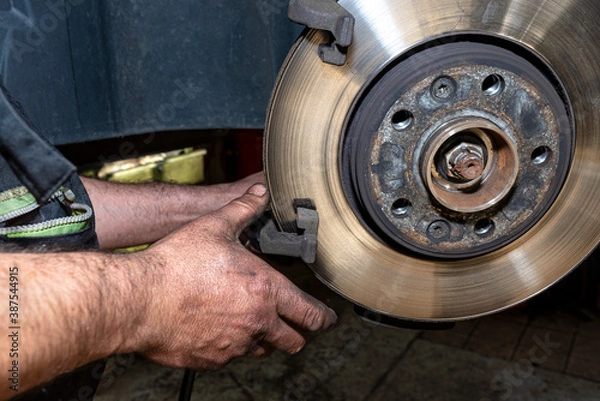 Fototapeta A car mechanic pulls a brake caliper in a car standing on a car jack in the workshop.