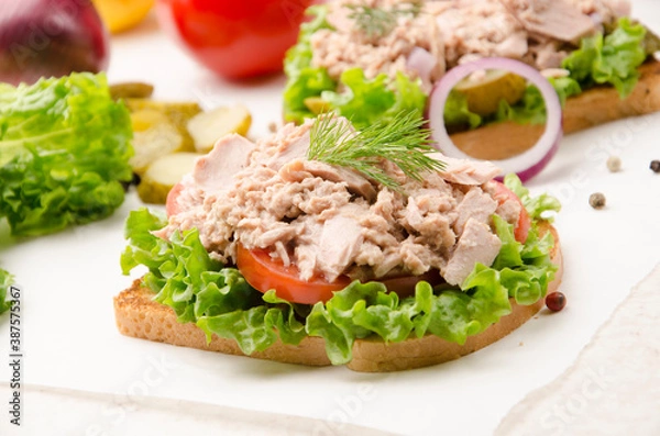 Fototapeta Tuna sandwiches with lettuce tomatoes and onions on parchment paper