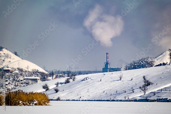 Fototapeta High and wide chimney, a pipe with a large amount of smoke and substances released into the atmosphere. Part of a factory or enterprise that pollutes the environment in a snowy and frosty winter near 