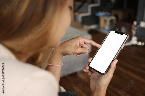 Fototapeta Asian woman holding a cell phone with a white screen in the coffee cafe. Smartphone on hand with clipping path.