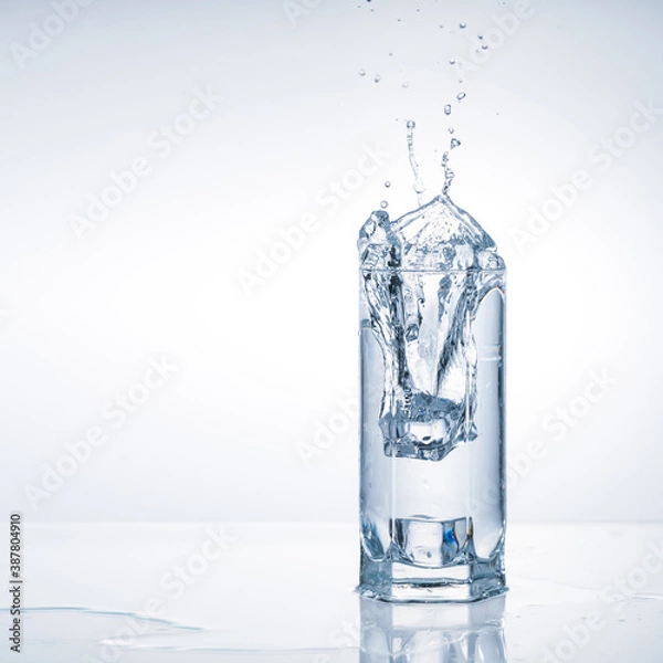 Fototapeta Ice cube falling in glass water. Splashes on light blue background with copy space