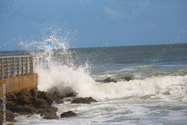 Fototapeta Waves crashing onto the pier with a fisherman barely visible in the wake