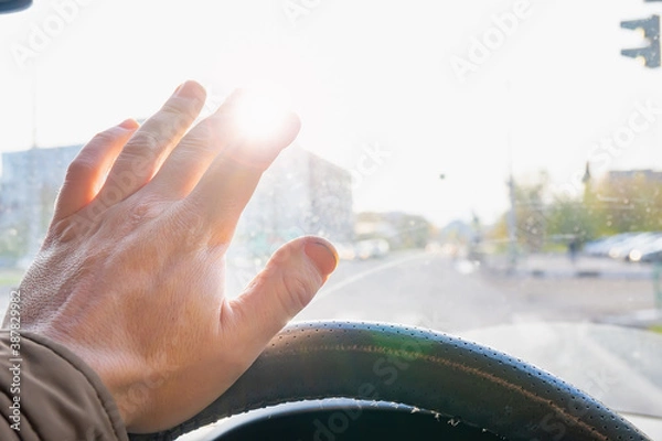 Fototapeta the driver's hand and fingers at the wheel of a moving car cover the sun, which blinds the eyes and does not see the roadway