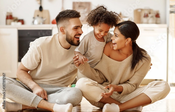 Fototapeta happy multiethnic family mom, dad and child  laughing, playing and tickles    on floor in cozy kitchen at home.