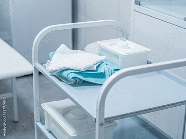 Fototapeta White medical operation small table bedside with towels, boxes on shelves in white interior, doctor's office. Workplace
