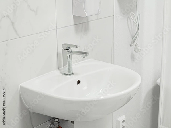 Fototapeta White new clean simple sink with metal shiny valve faucet in white interior of a medical clinic. Tiled wall in the background