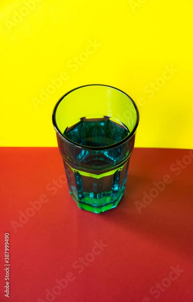 Obraz Glass with water on yellow and red background. selective focus. concept of light refraction. abstract object
