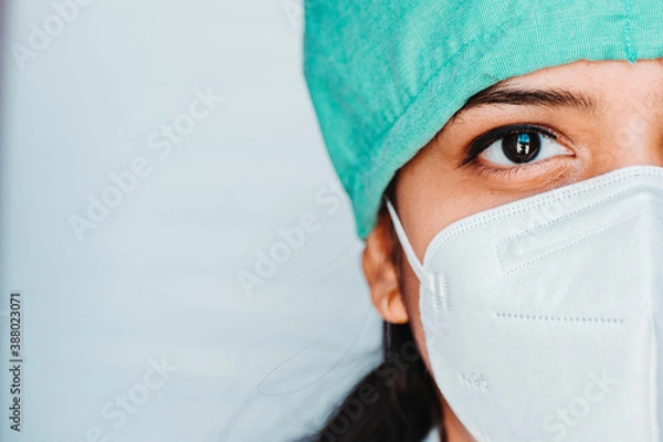 Obraz Close up portrait of half face of  young Indian female surgeon doctor in Emergency room wearing mask and cap during corona virus pandemic