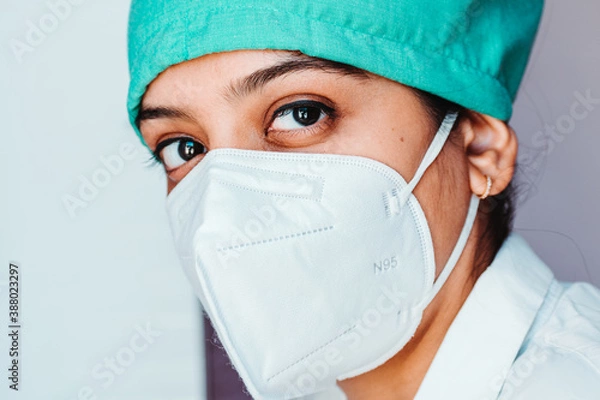 Obraz Close up portrait of young Indian female surgeon doctor in Emergency room wearing mask and cap during corona virus pandemic